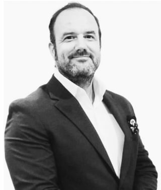 Black and white professional portrait of a man with beard wearing a dark blazer over white dress shirt