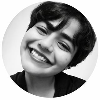 Black and white circular portrait of a smiling person with short dark hair tilting their head slightly