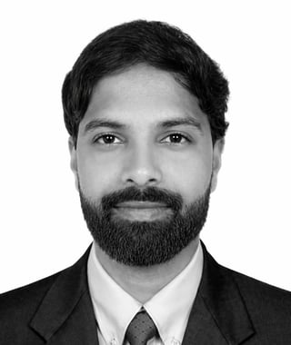 Black and white professional headshot of a man with dark hair and beard wearing a dark suit and tie