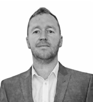 Black and white professional headshot of a man wearing a gray blazer and white shirt against a white background