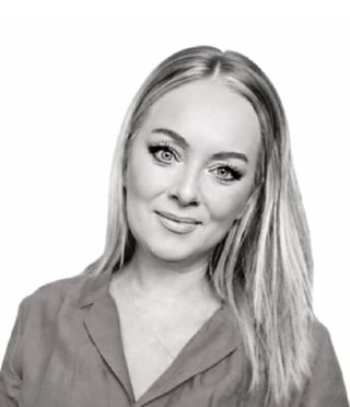 Black and white portrait of a woman with long blonde hair wearing a blazer, smiling at the camera against a white background