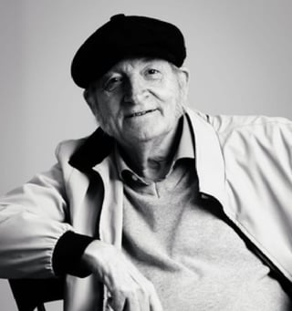 Black and white portrait of an elderly man wearing a black beret and white jacket, smiling at the camera